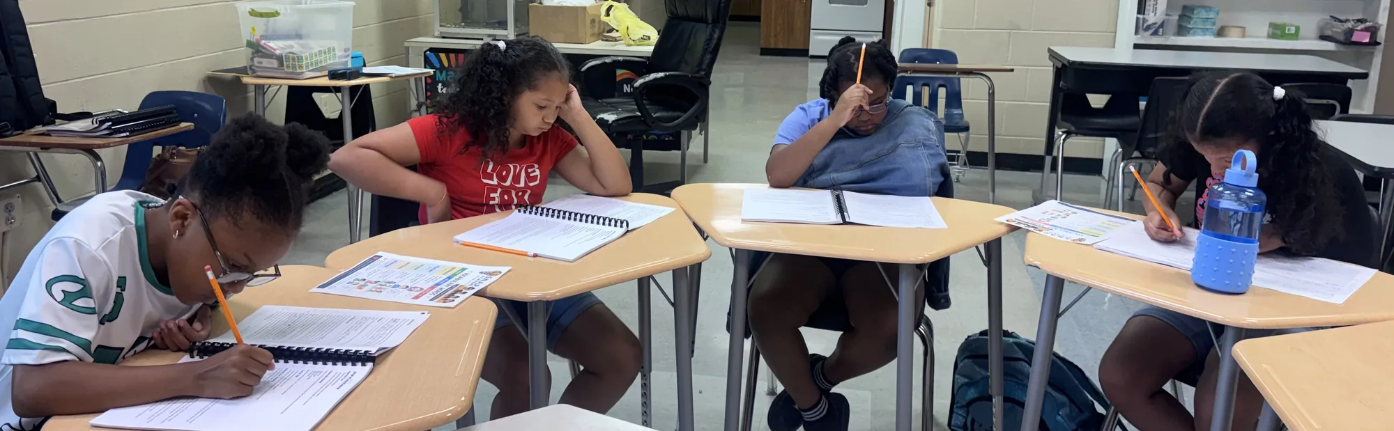 Students along a row of desks with their notebooks open, heads down and working through the morning’s pages.